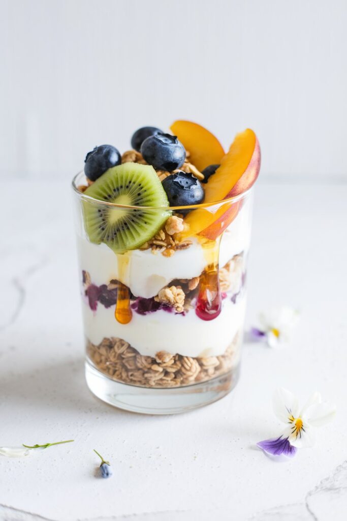 A clear glass layered with creamy yogurt, granola, and an assortment of colorful spring fruits like kiwi, 