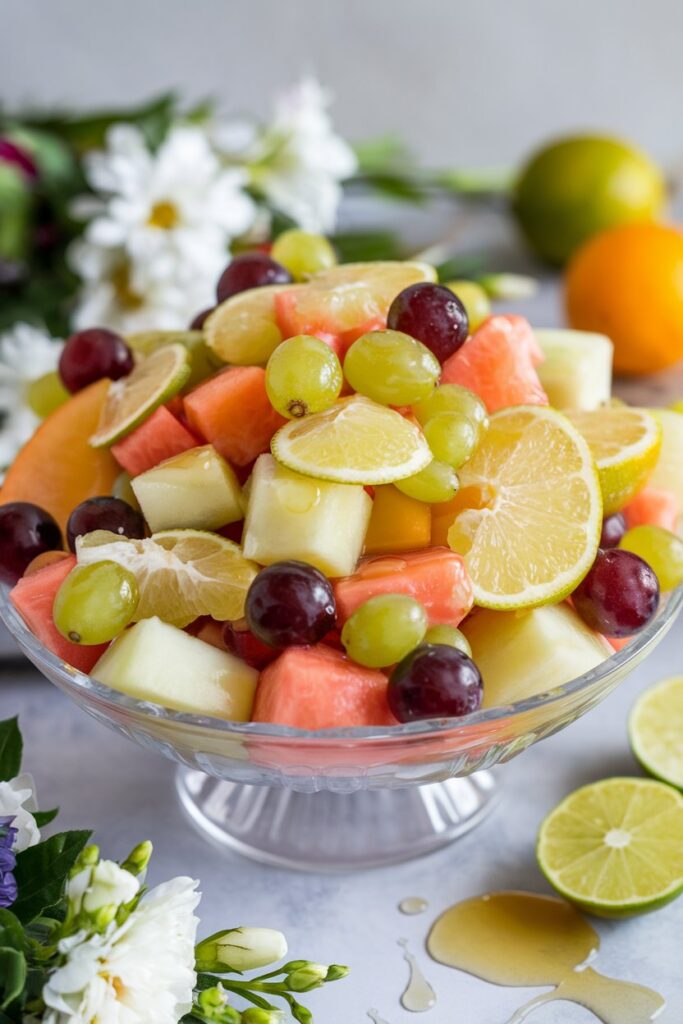 A vibrant bowl of fruit salad including melons, grapes, and citrus segments, lightly glazed with a honey-lime dressing.